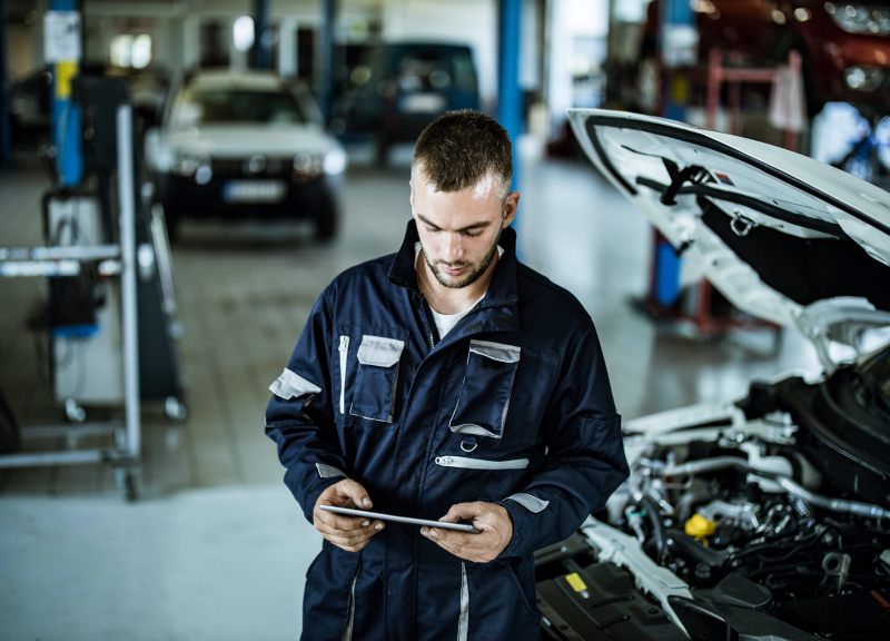 Mécanicien effectuant des diagnostics sur une tablette à côté du capot ouvert d'une voiture